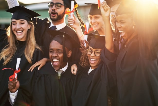 A group of students in graduation caps and gowns cheers.